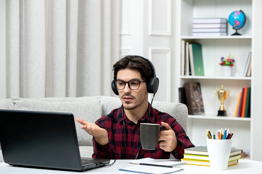 Man in headphones on a video call at his laptop, explaining something with his hands